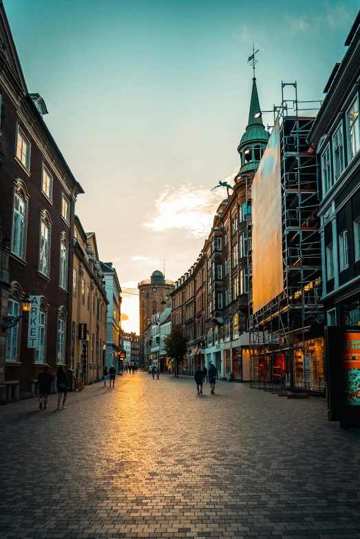 the sun sets behind a row of old buildings and people walk