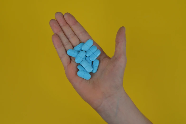 blue pills sitting on the palm of a person's hand