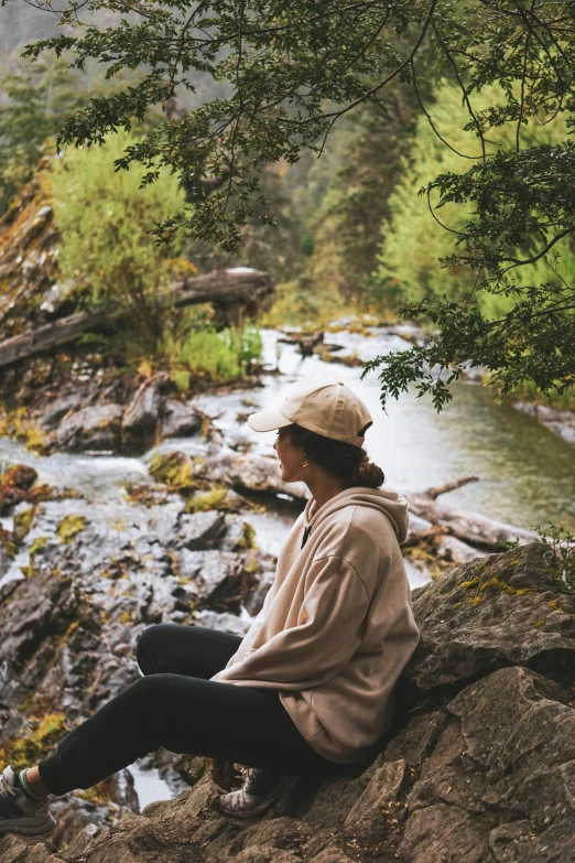 a woman sitting on top of a rock near a river