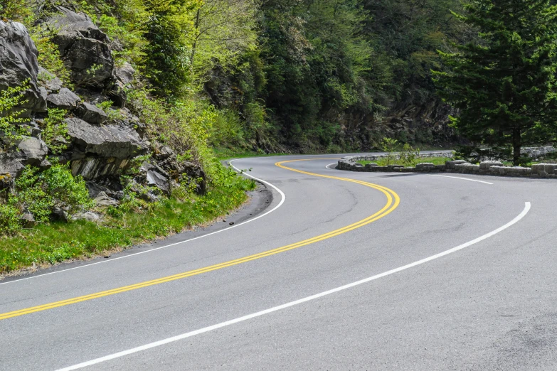 a paved highway in a wooded area, with large rocks on either side