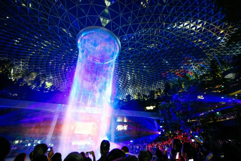 a large white fountain inside a building surrounded by lots of people