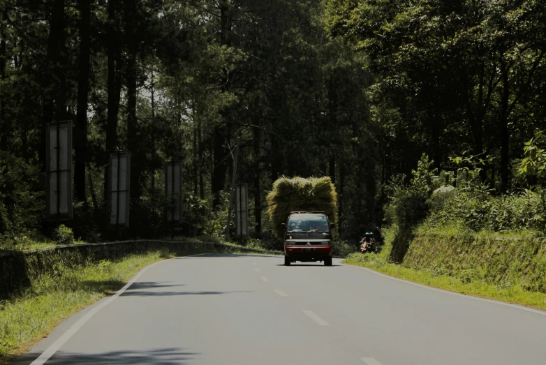 a van is driving down the road with hay on its roof