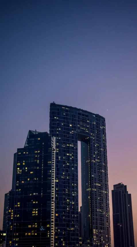 a high rise building illuminated by lights in front of a purple sky