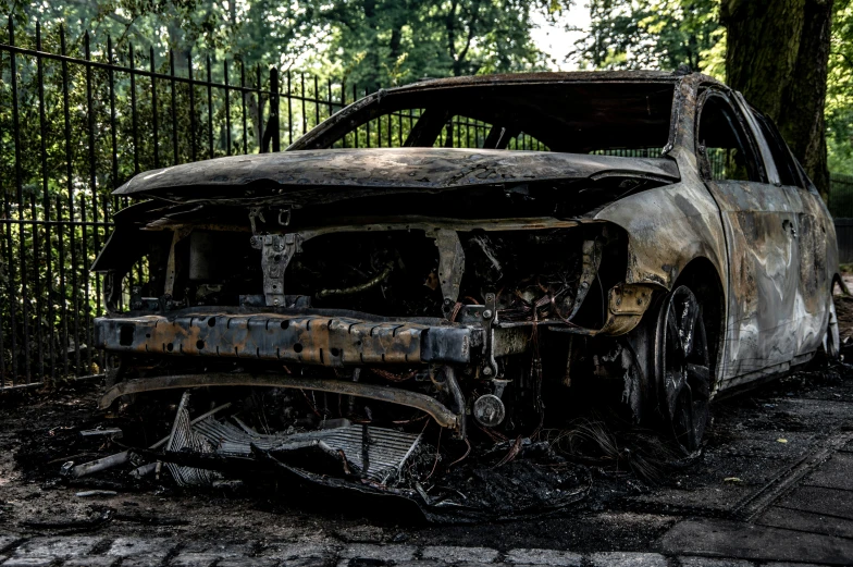 a burned car in a dirty lot by trees