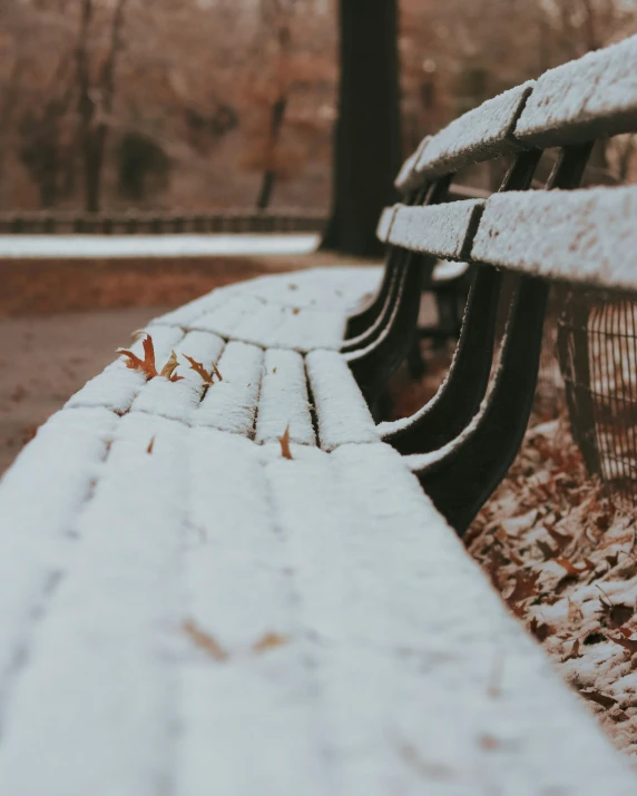 an empty park bench covered in snow during a winter day