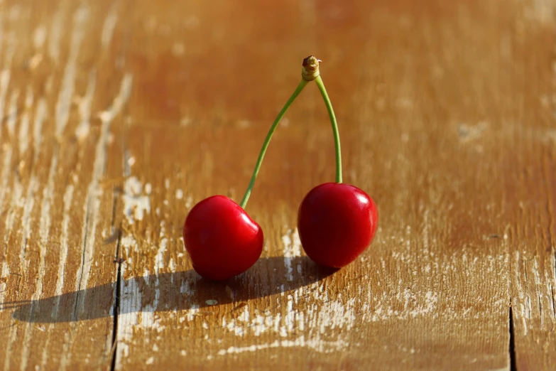 two cherries sit on top of a wooden surface