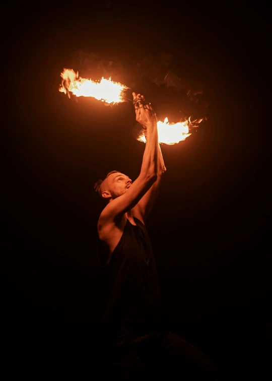 fire performer holding torches on dark background