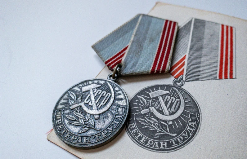 two medals on a table next to a pair of red and white striped ribbons