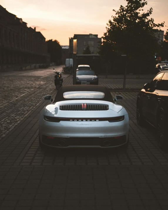 a silver car parked next to other cars on a brick road