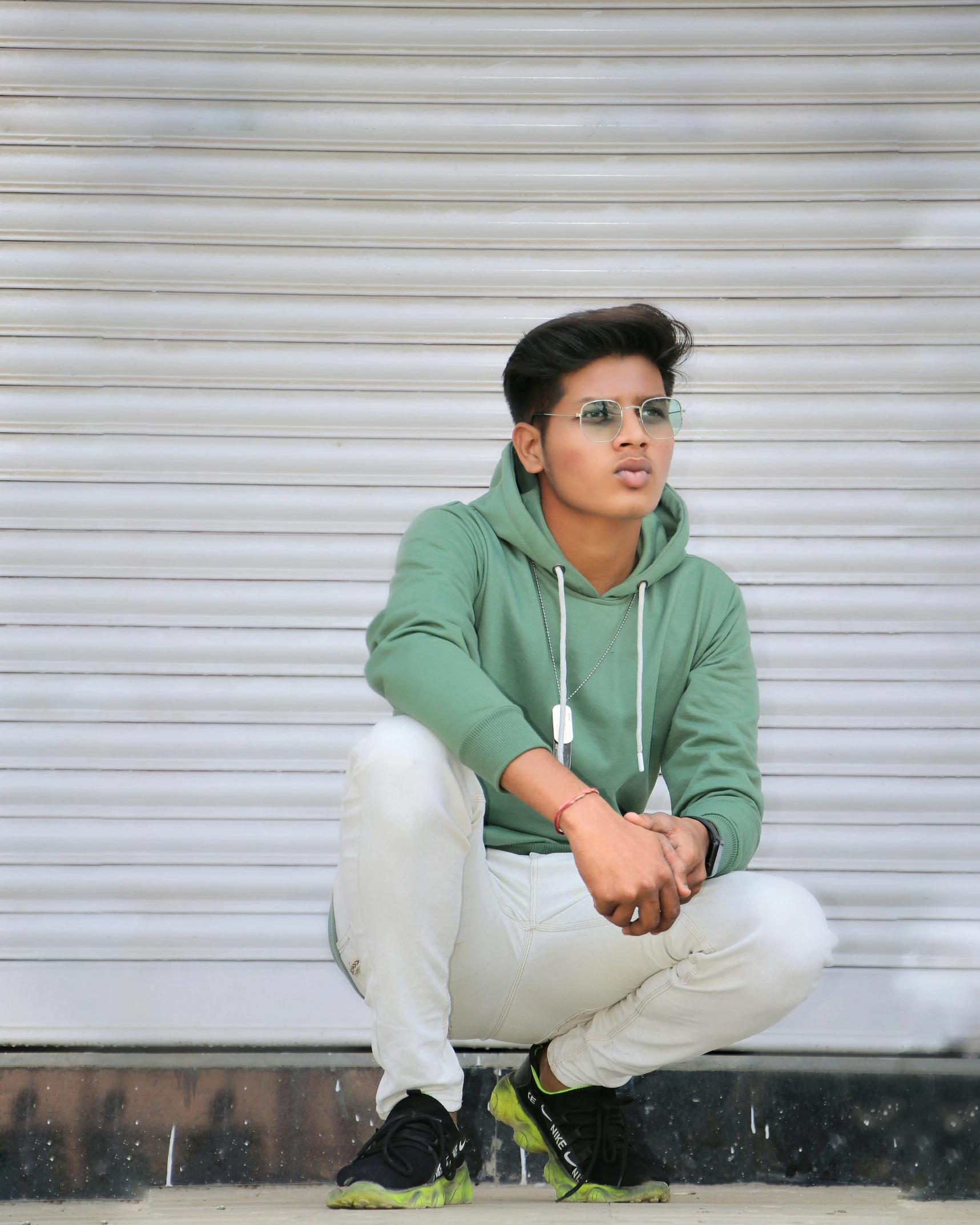 a boy in a green jacket crouches against a wall