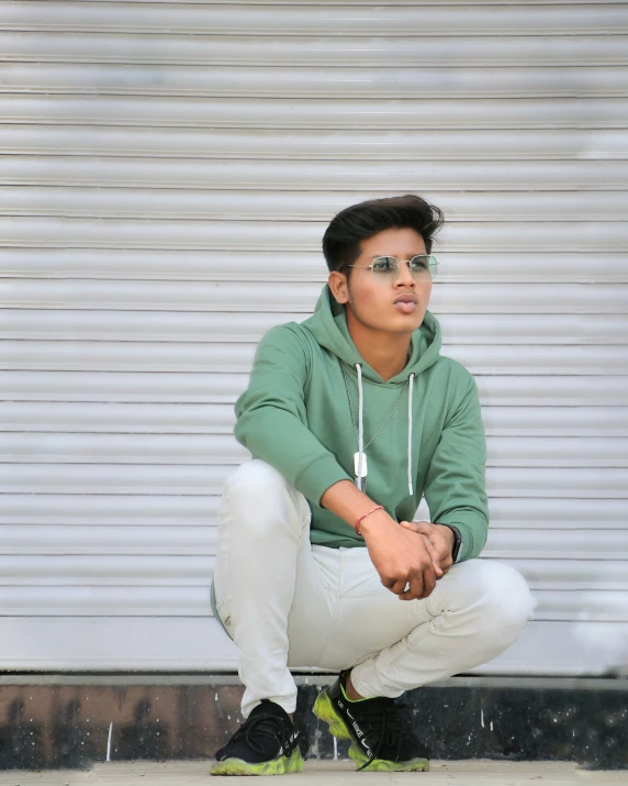 a boy in a green jacket crouches against a wall