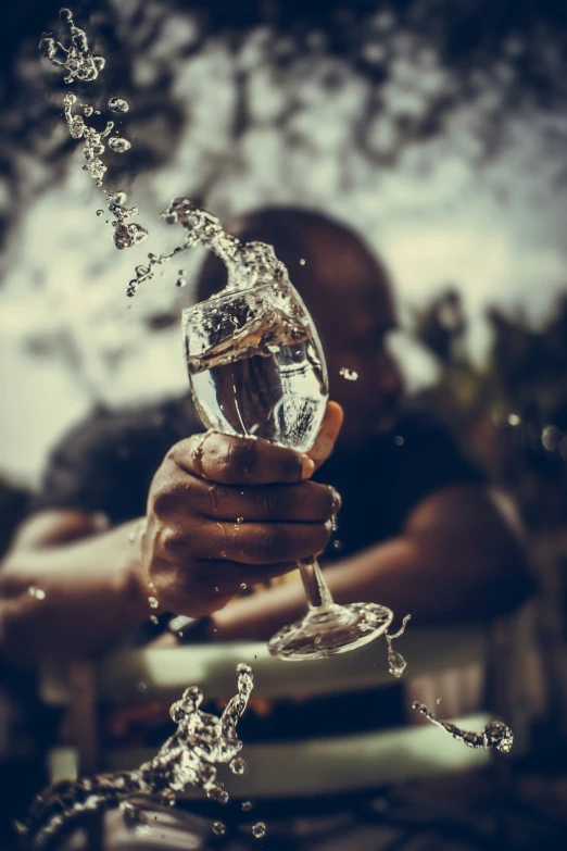 a hand pouring water into a glass with a person standing in the background