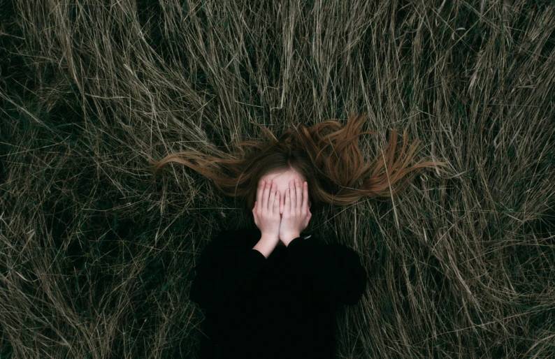 woman in black top laying with her head in tall grass