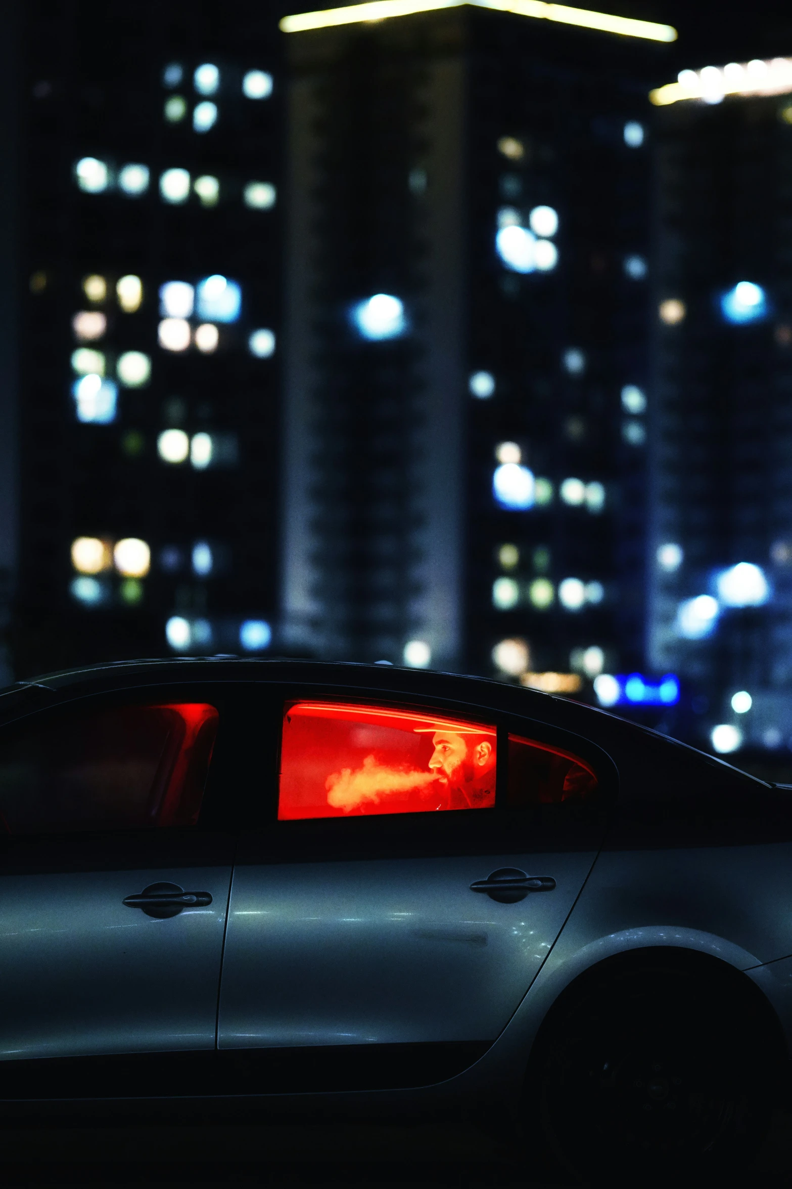 the back of a silver car with a red rear light on in a city at night