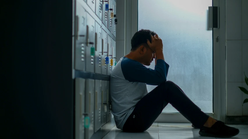 a man sitting on the floor and looking at a wall with multiple lockers