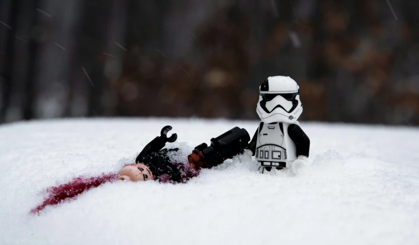 a star wars figure laying in the snow near a dead person