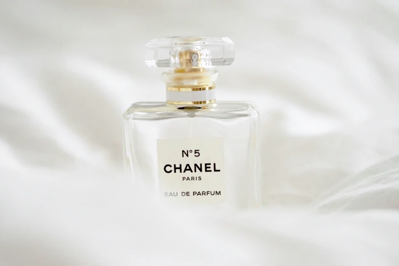 a white bed topped with a bottle of chanel no 5