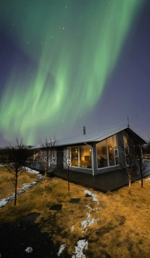 a small cabin is under the green lights of the aurora