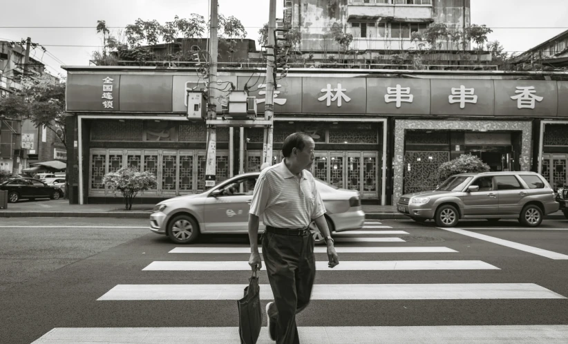 a man with a bag crosses a street in front of a business