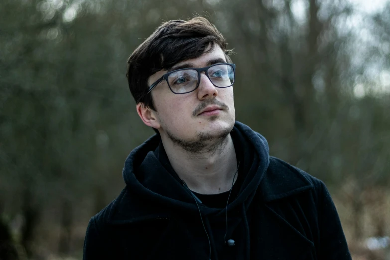 a young man wearing glasses standing in the woods