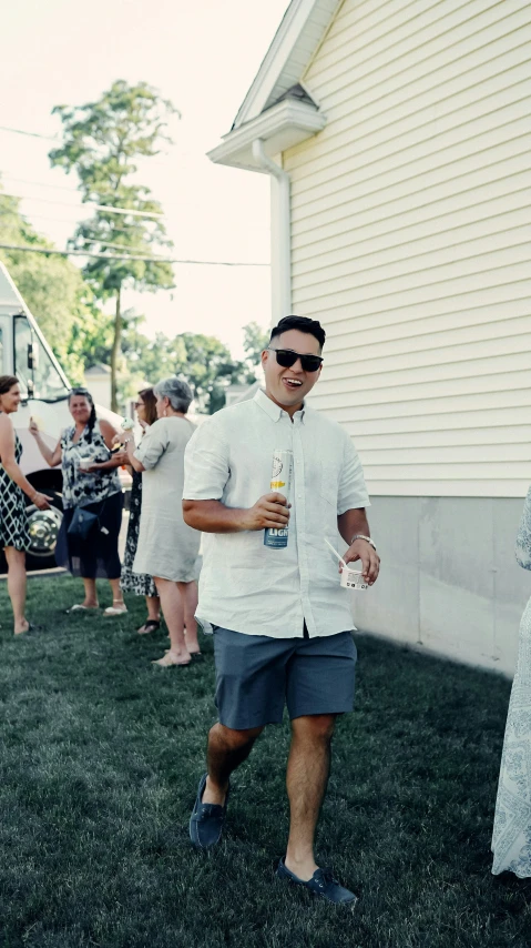 a man in a white shirt and blue shorts stands in the yard holding two beer