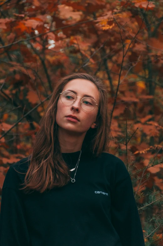 a woman in glasses, with a red and yellow fall tree behind her