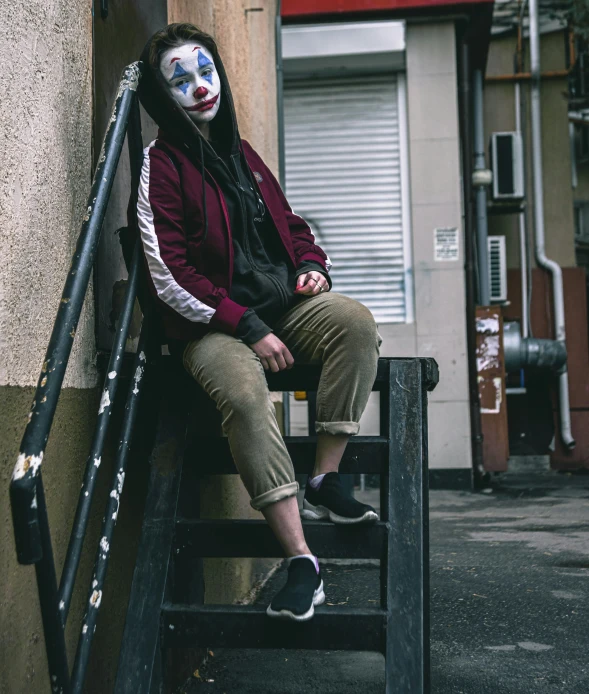 a clown with makeup sitting on the steps near a building