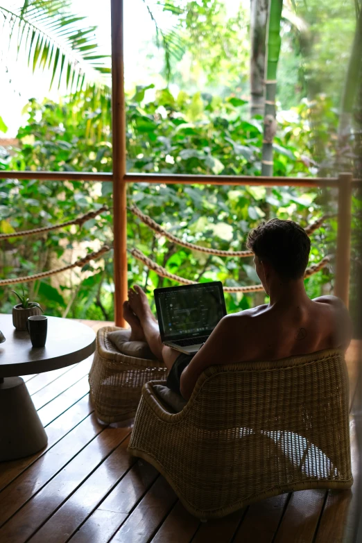 a man sitting on a wicker chair using a laptop computer