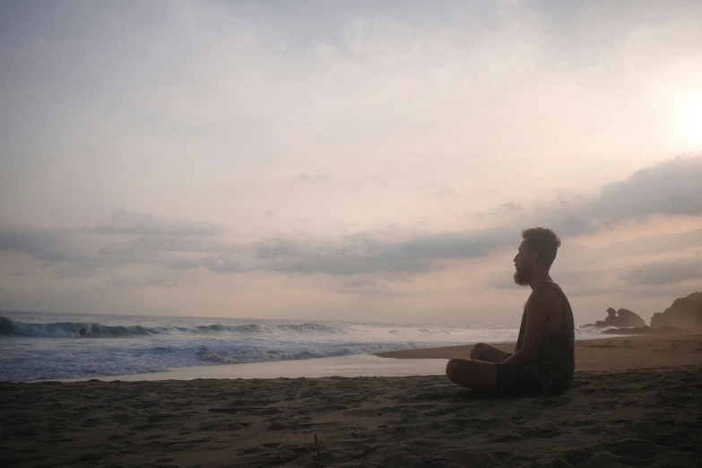 the man sits on the sand near the water