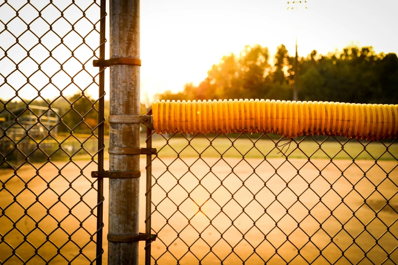 a close up of a chain link fence with a park and basketball court in the background