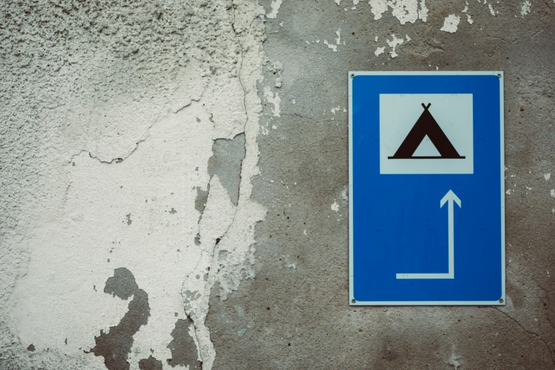 a blue sign pointing right at the corner of a wall