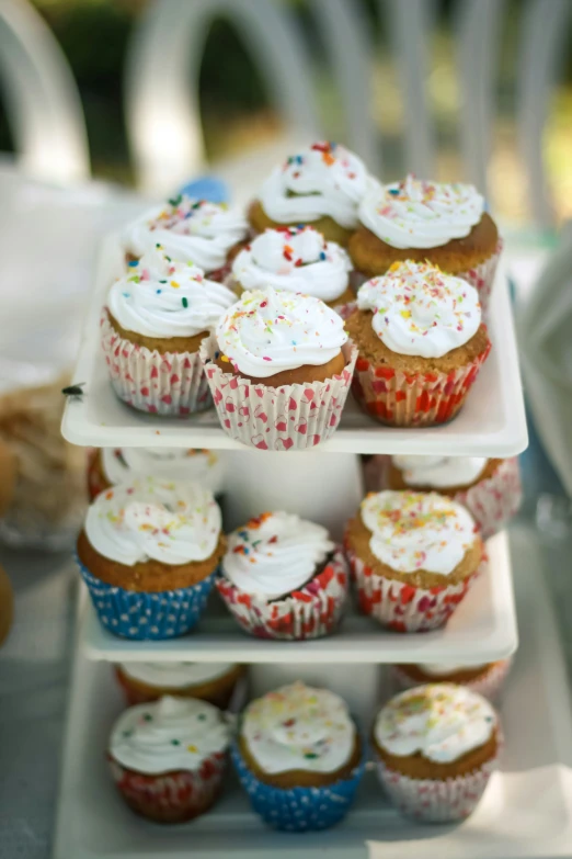 cupcakes on three tiers with one muffin topped with white frosting and sprinkles