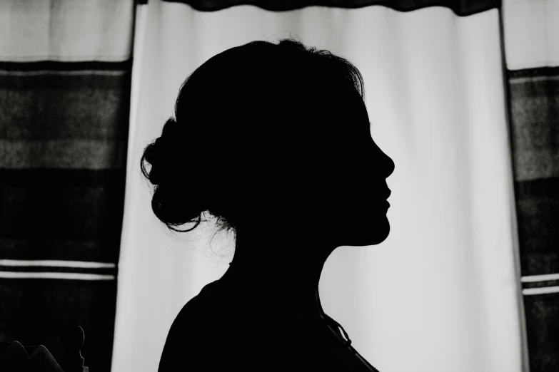 the silhouette of a woman next to the curtains