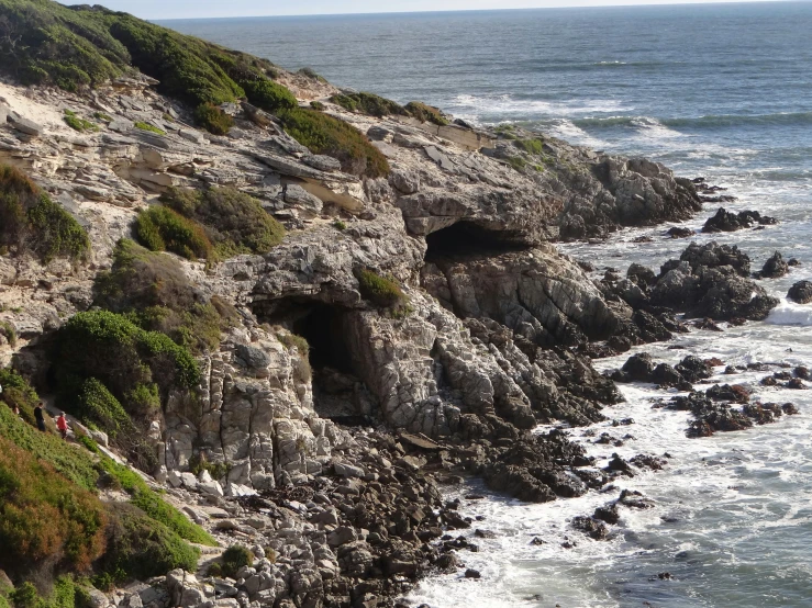 a rocky cliff overlooks the ocean with two small caves carved into them