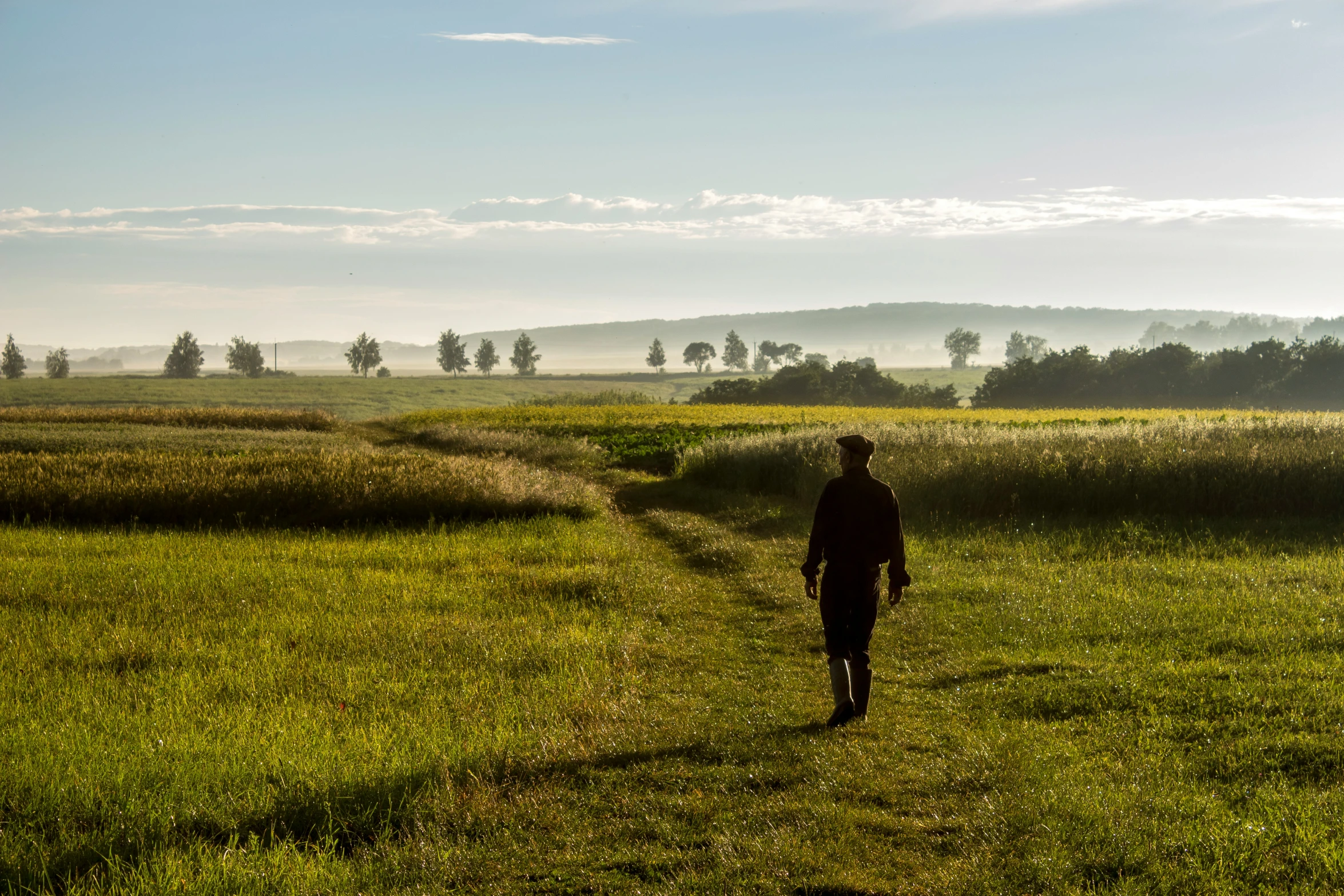 the man is walking alone across the field with no one in sight