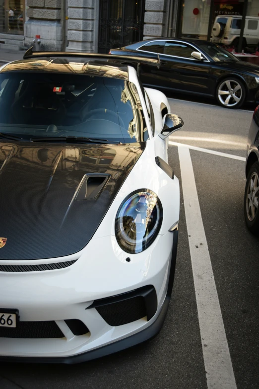 a white sports car with hood up on a city street