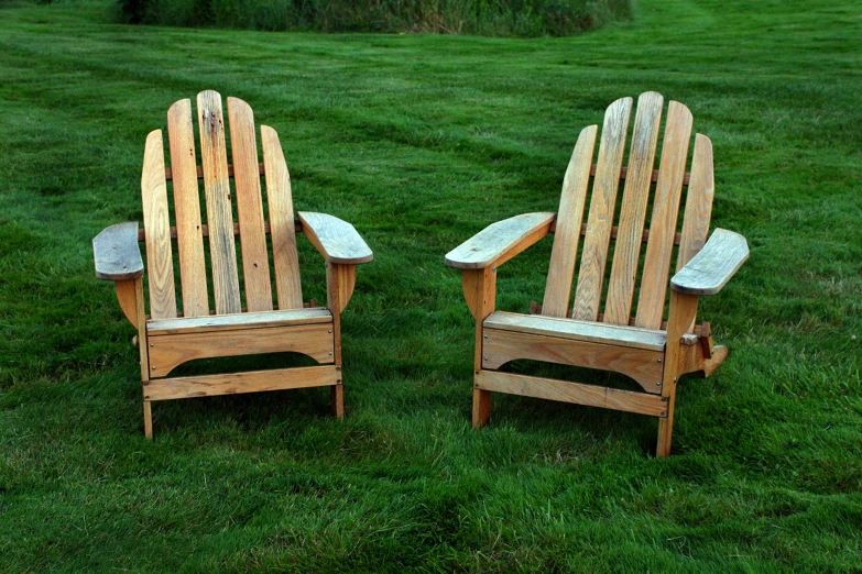a pair of wooden chairs sit on the grass