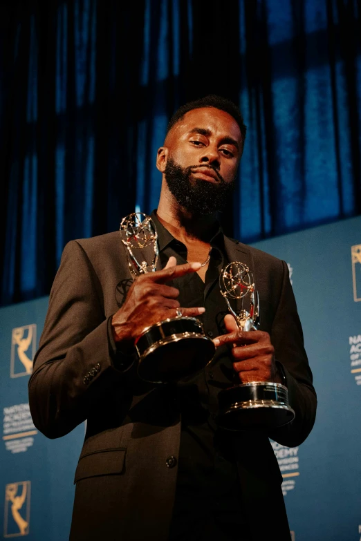 a black man standing holding two awards in his hands