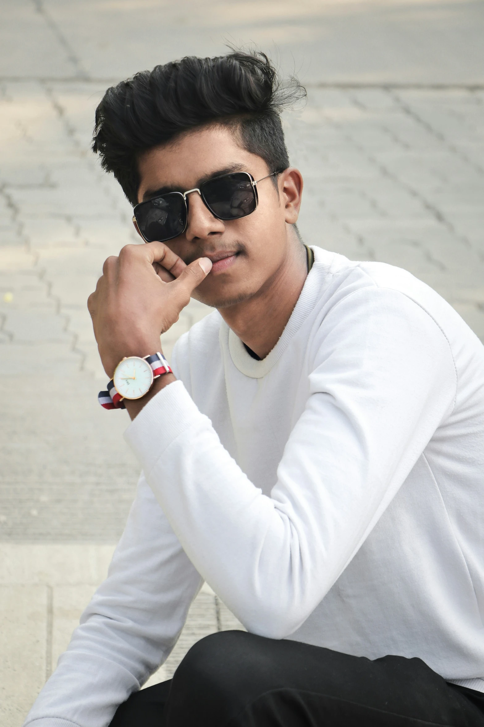 a man sitting on a bench wearing sunglasses and holding a watch