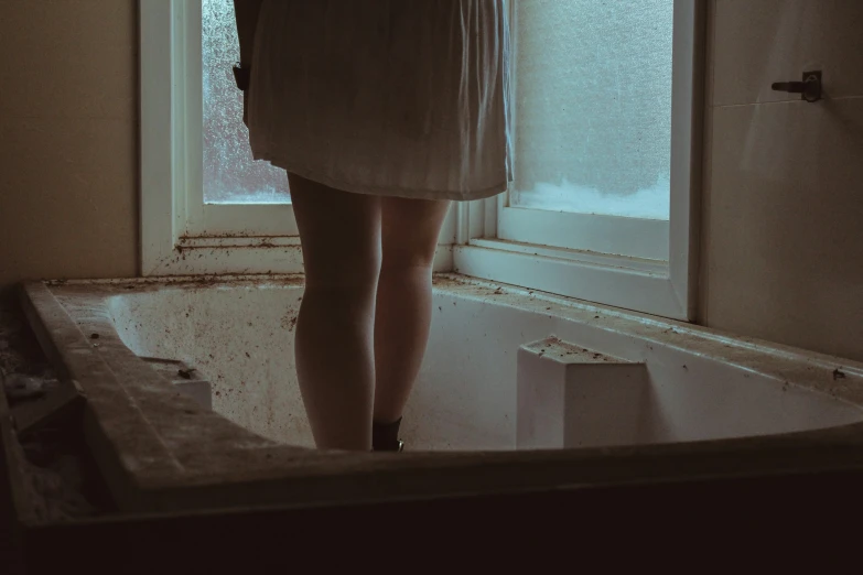 a person stands in a bathtub looking out a window