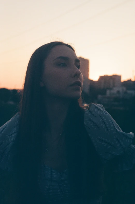 a  with long hair is standing in front of a sunset