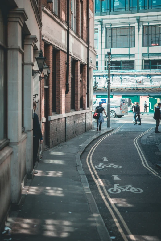 people are standing on the side of an alley as traffic passes by