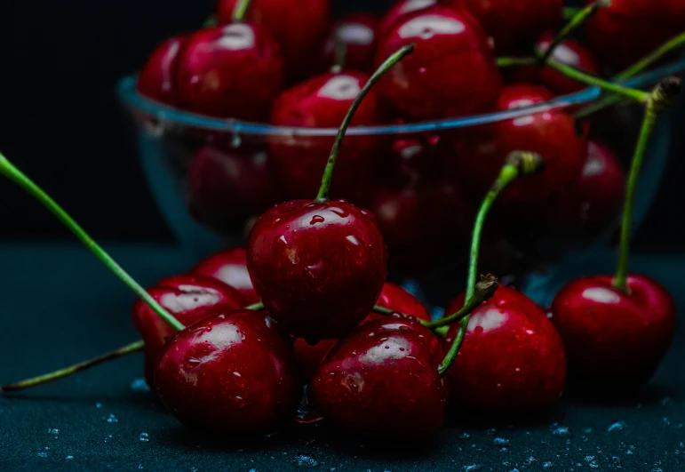 cherries sit on the table next to a clear glass bowl