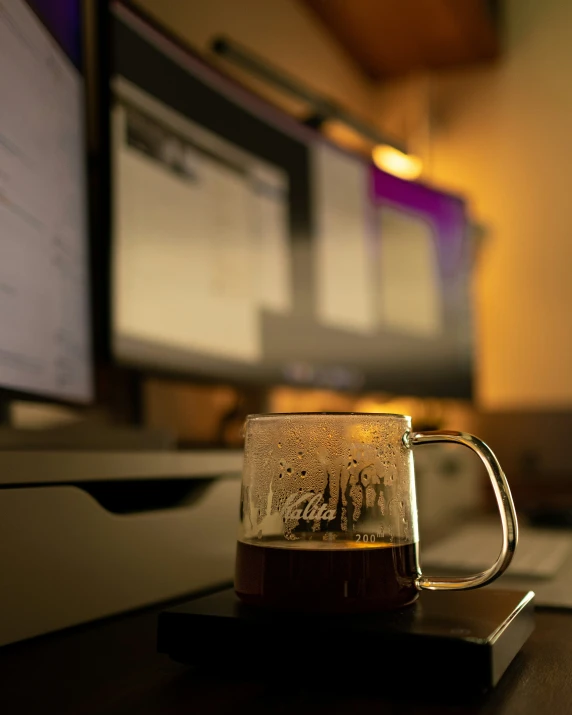 a glass mug on top of a table with a television in the background