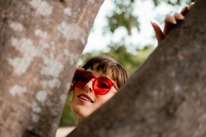 a  is wearing red sunglasses and standing behind the tree