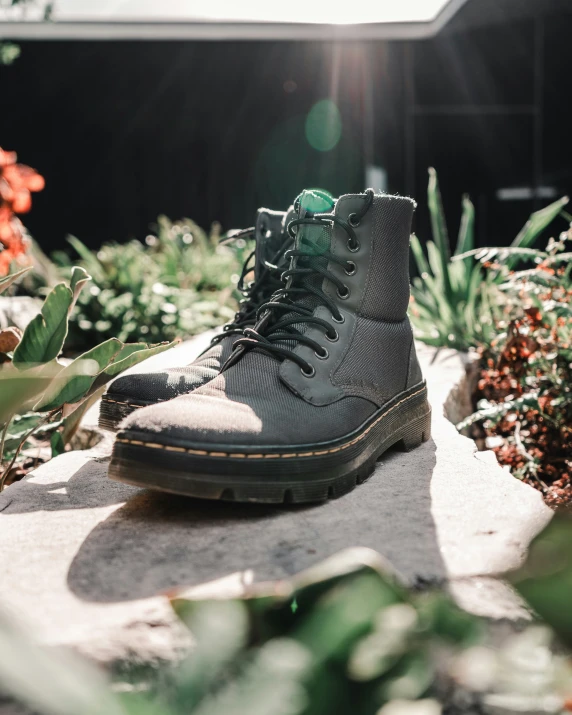 a pair of grey combat boots sits on a stone sidewalk among colorful flowers