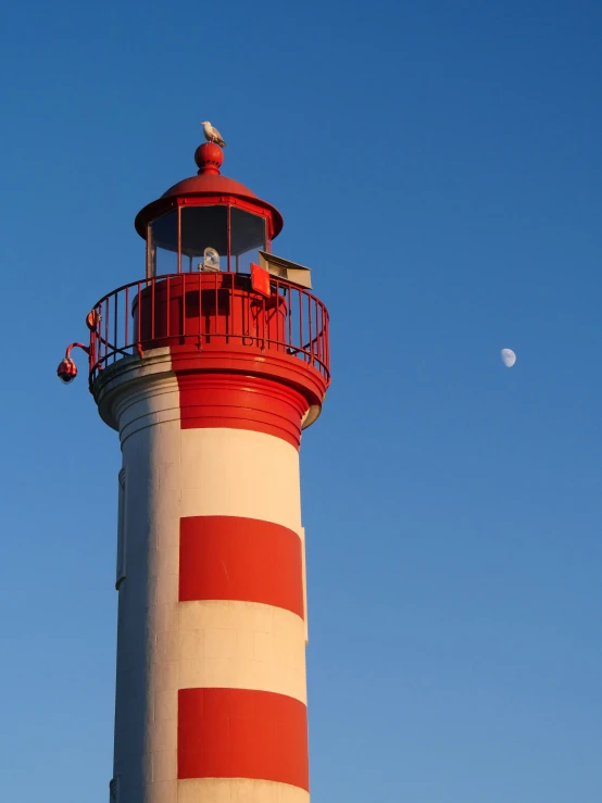 an image of a red and white lighthouse under the moon