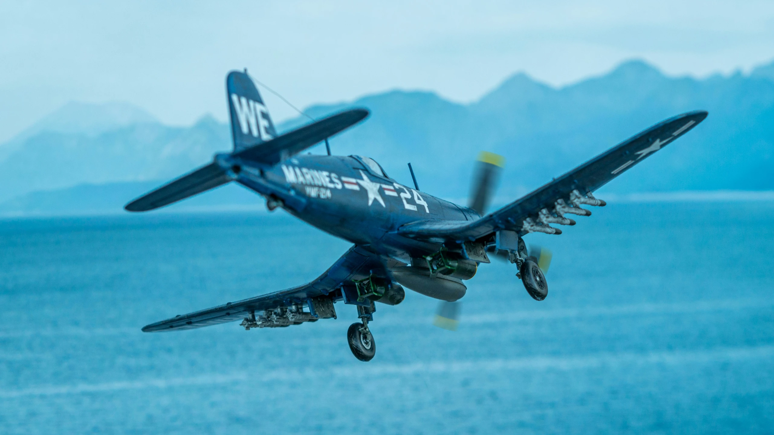 an airplane flying over the ocean with mountains in the background