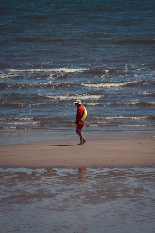 the man is walking away from the water carrying his surfboard