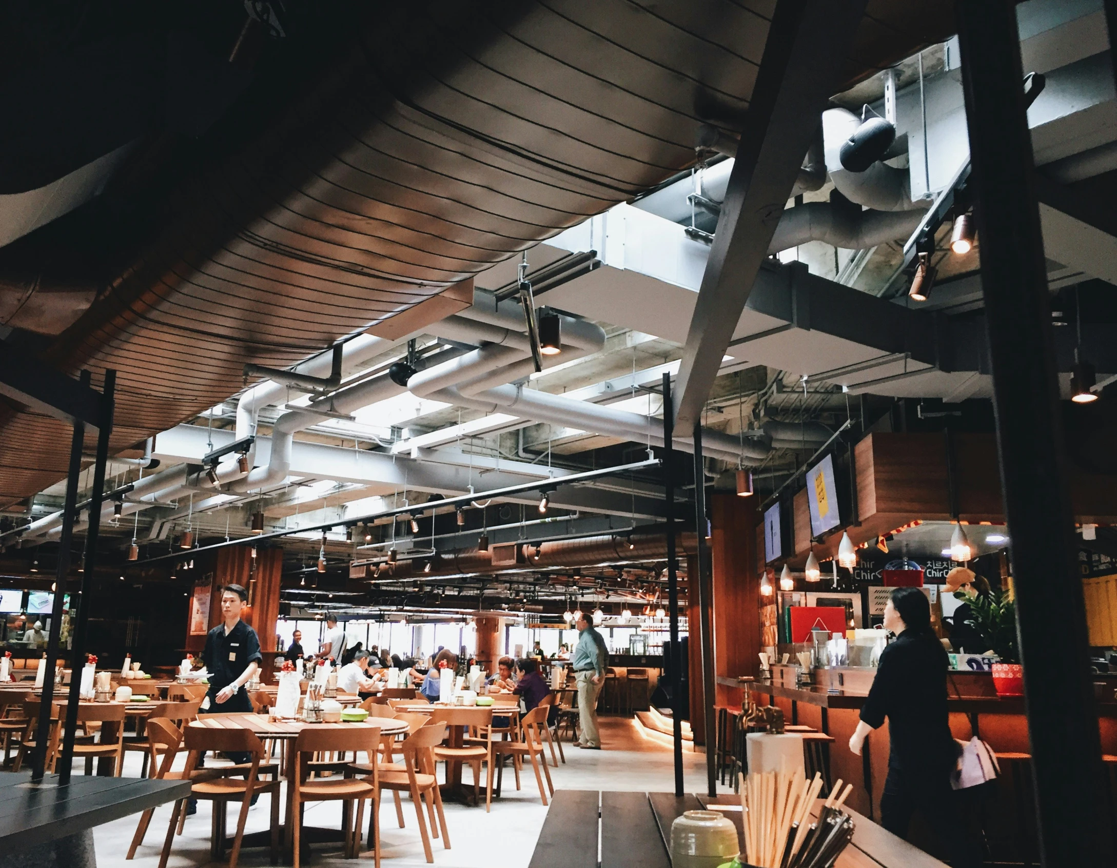 inside the restaurant with wood chairs and people standing around